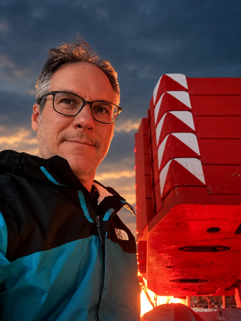 Tomaz Cavalieri ao lado de equipamento de uma embarcação ao entardecer
